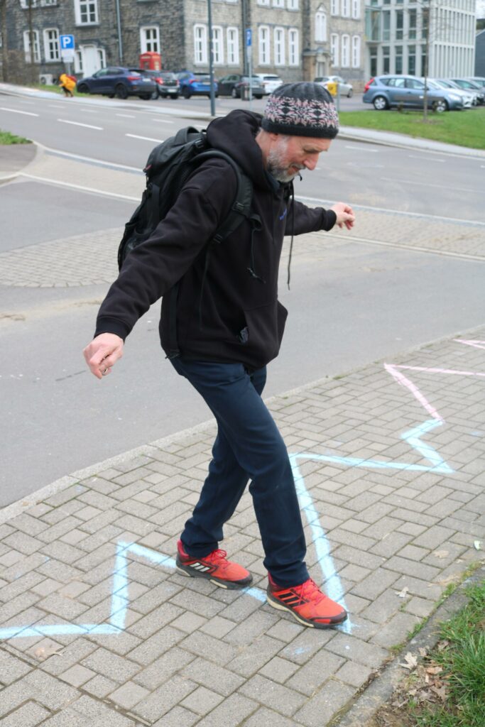 Junger Mann balanciert auf einem Zickzack-Muster auf dem Bürgersteig.