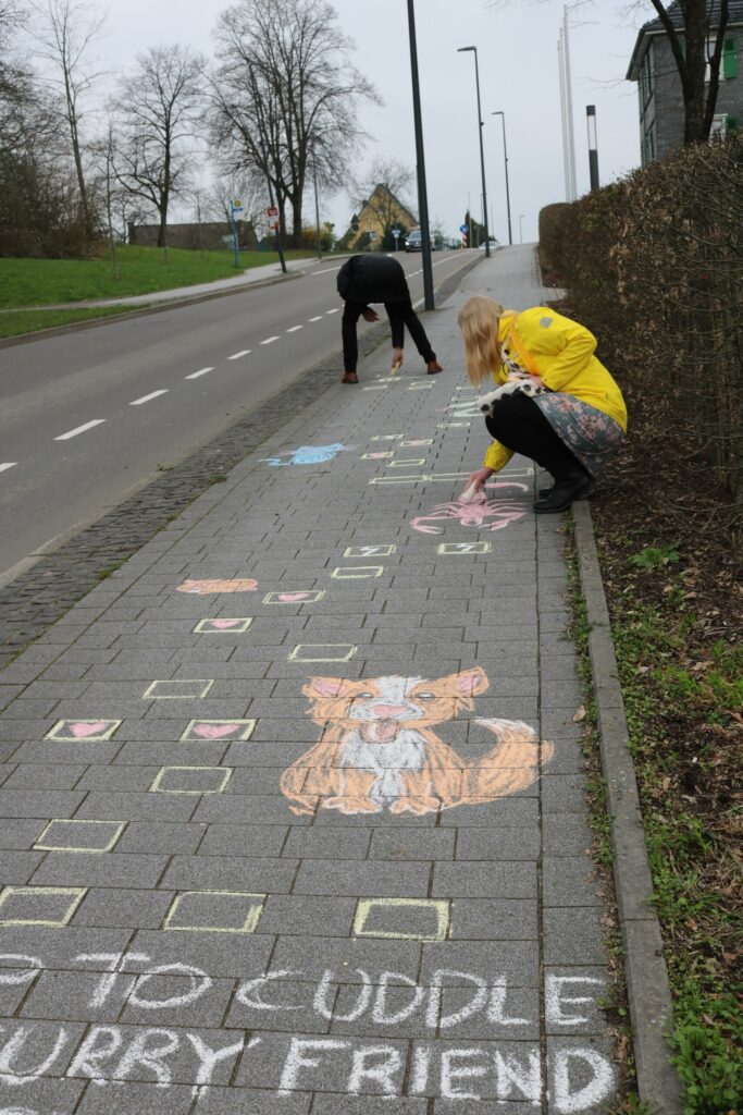 Kinder malen mit Kreide bunte Bilder und Schriftzüge auf den Gehweg.