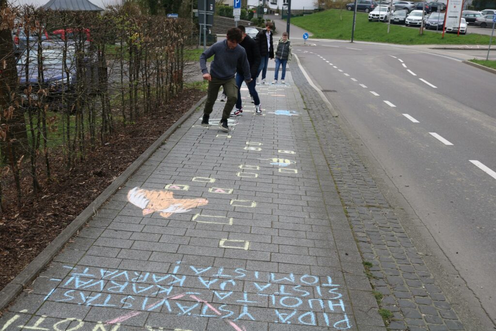 Schüler zeichnen mit Kreide bunte Bilder und Schriftzüge auf dem Bürgersteig.