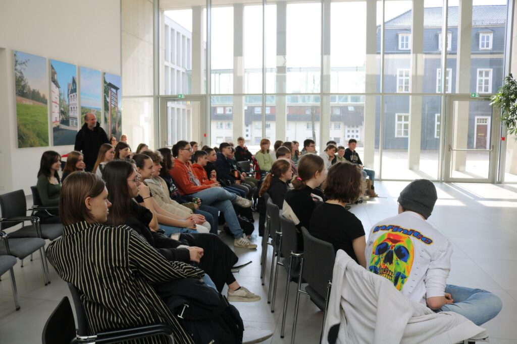 Schüler sitzen in einem hellen Raum und hören einem Vortrag zu.