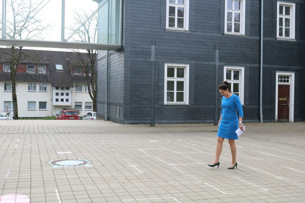 Frau in blauer Kleidung geht über einen Platz vor einem modernen Gebäude.