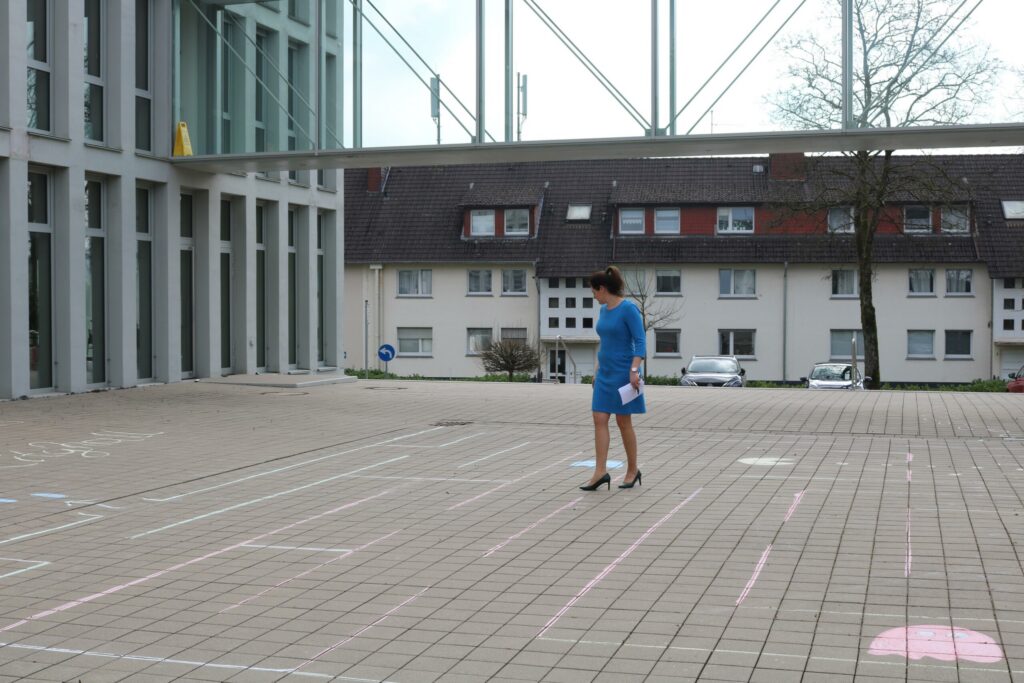 Frau in einem blauen Kleid steht auf einem Platz mit Straßenkreidezeichnungen.