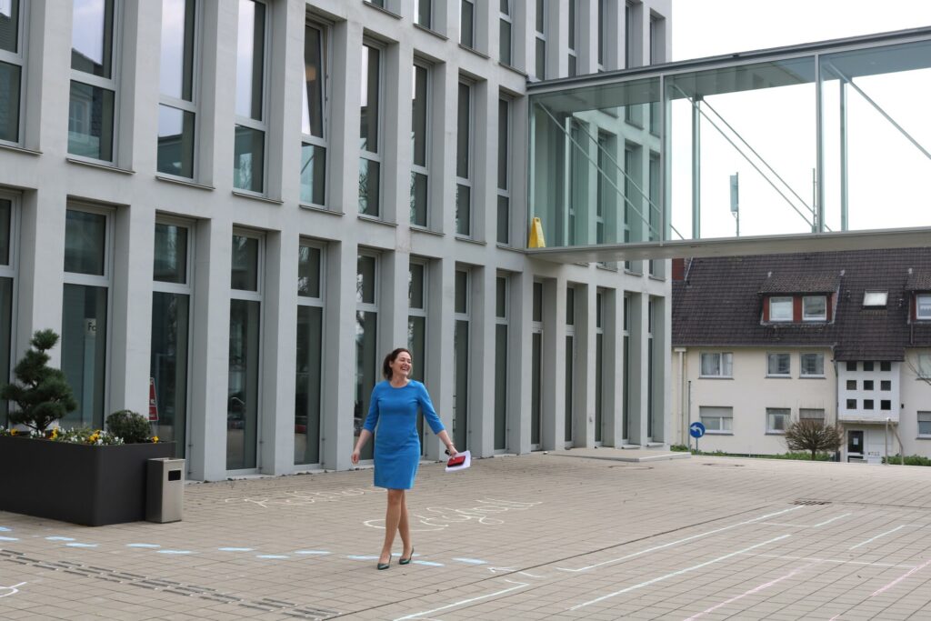 Frau in blauer Kleidung steht vor modernen Gebäuden und einer Brücke.