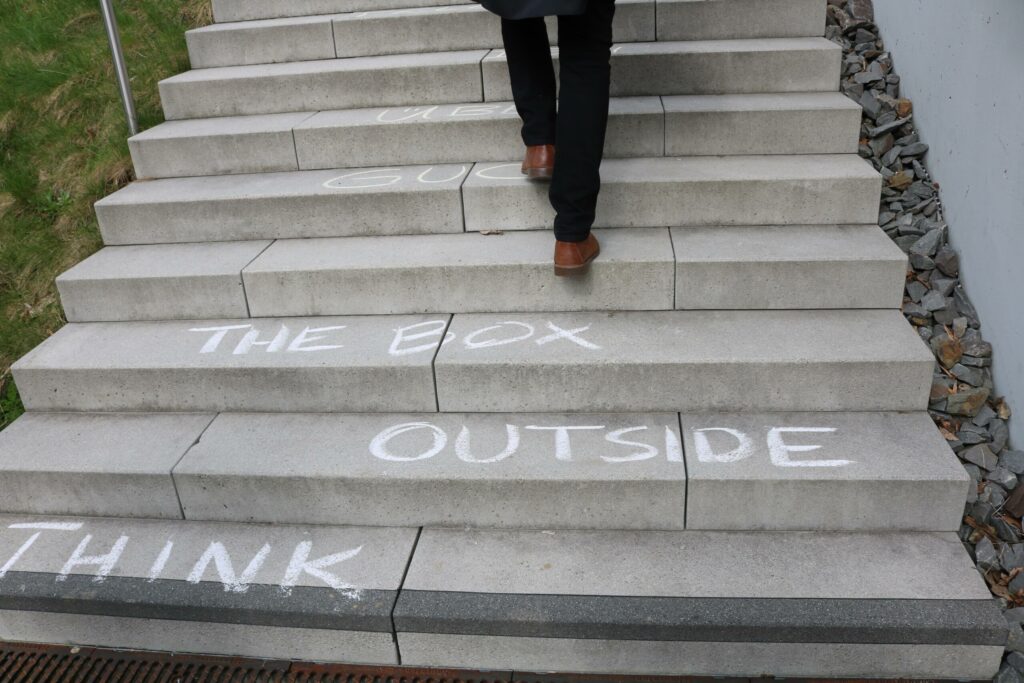 Eine Person geht eine Treppe hinauf, auf den Stufen steht: "THINK OUTSIDE THE BOX".
