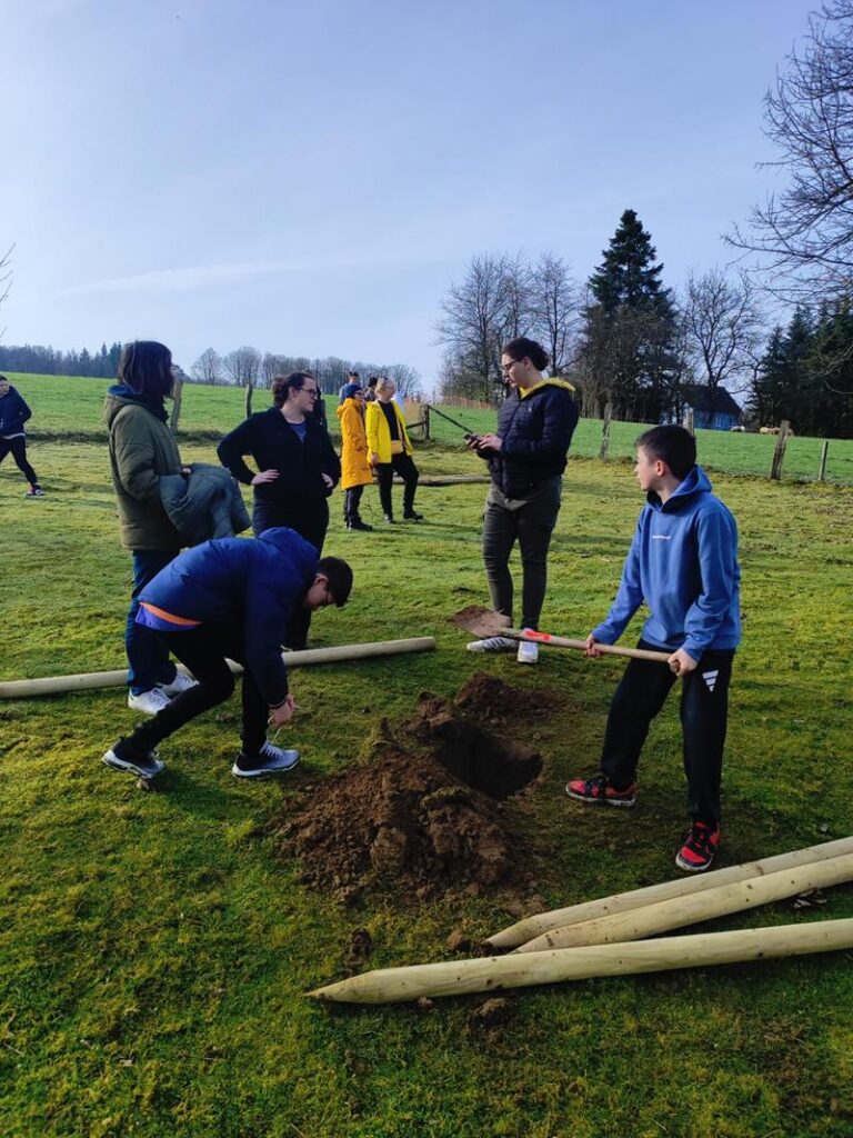 Schülerinnen und Schüler pflanzen einen Baum auf einer Wiese.