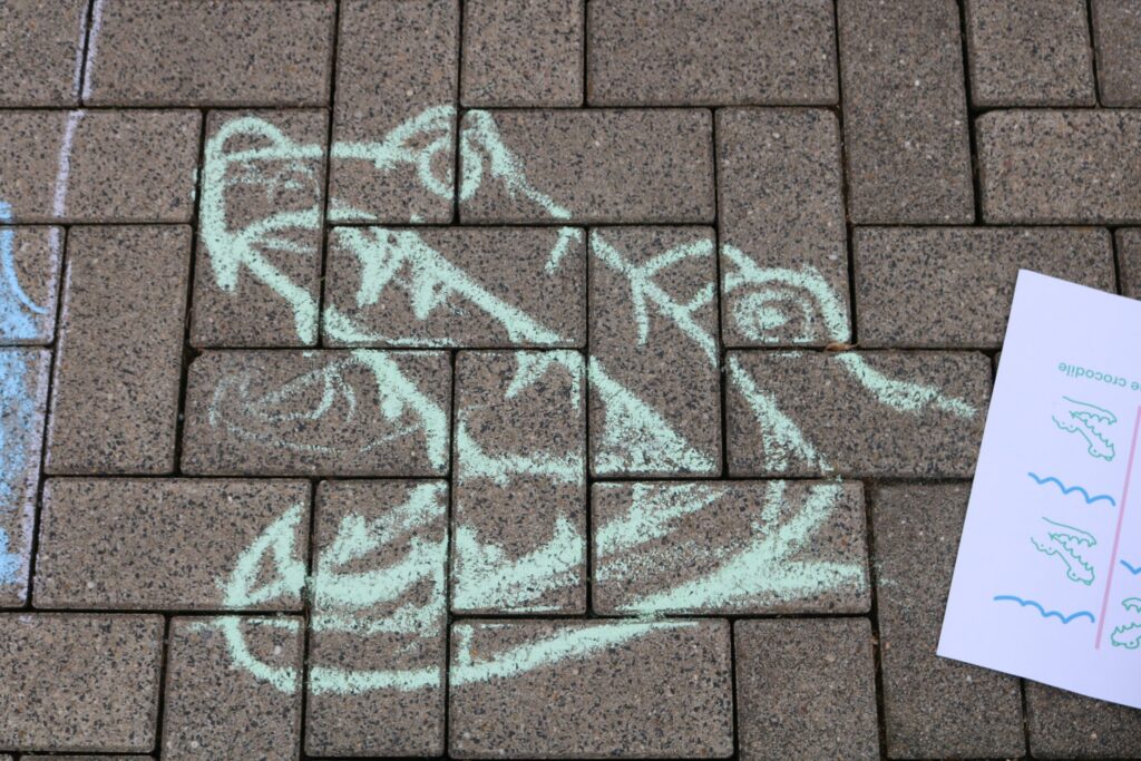 Kreidezeichnung eines Krokodils auf einem gepflasterten Boden.