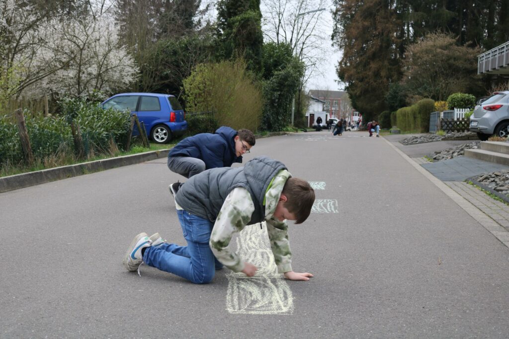 Zwei Kinder knien auf einer Straße und zeichnen mit Kreide.