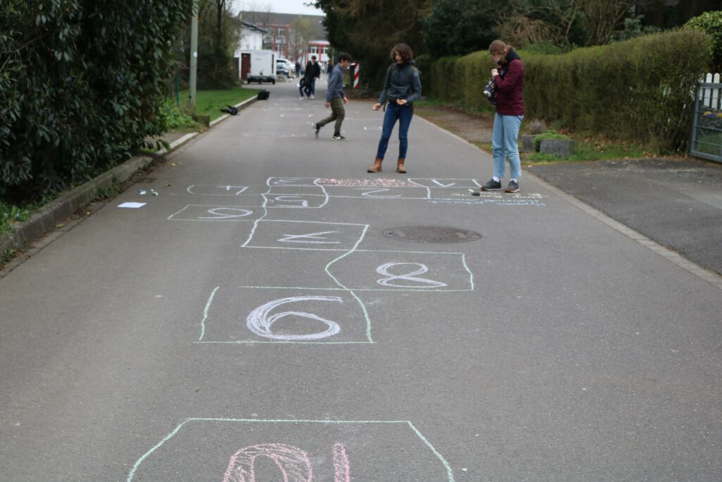 Kinder spielen auf einem mit Kreide bemalten Gehweg.