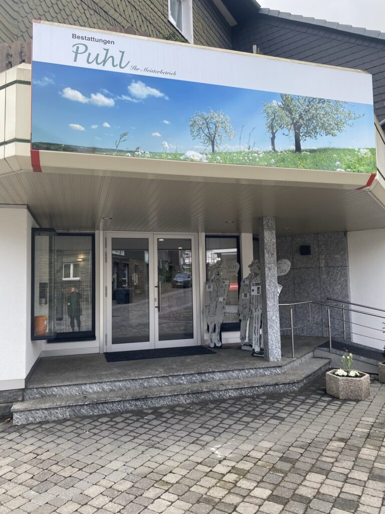 Eingang eines Gebäudes mit beschriftetem Vordach und dekorativen Elementen.