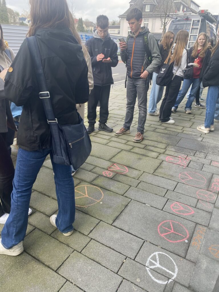 Schüler stehen auf einem Gehweg, umgeben von farbigen Kreidemalereien.
