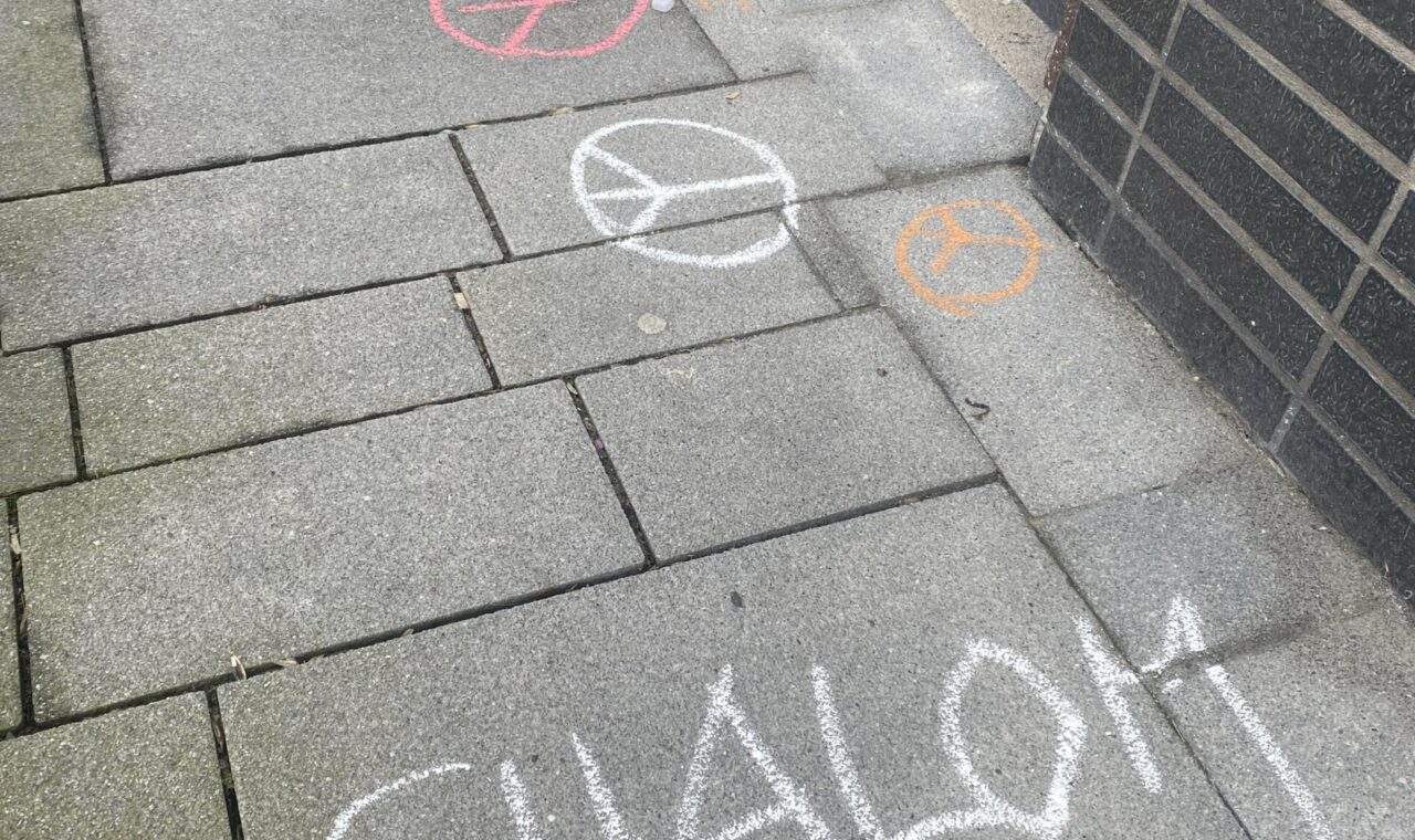 Kreidezeichnungen auf einem Gehweg, darunter Schriftzüge und Symbole.