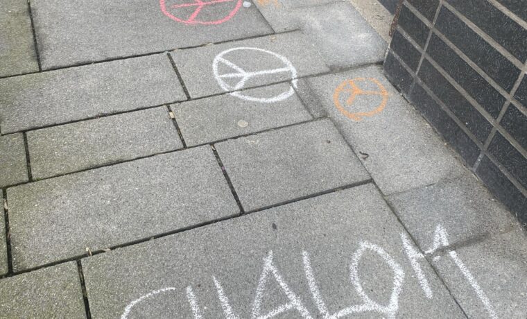 Kreidezeichnungen auf einem Gehweg, darunter Schriftzüge und Symbole.