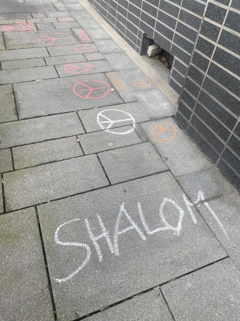Kreidezeichnungen auf einem Gehweg, darunter Schriftzüge und Symbole.