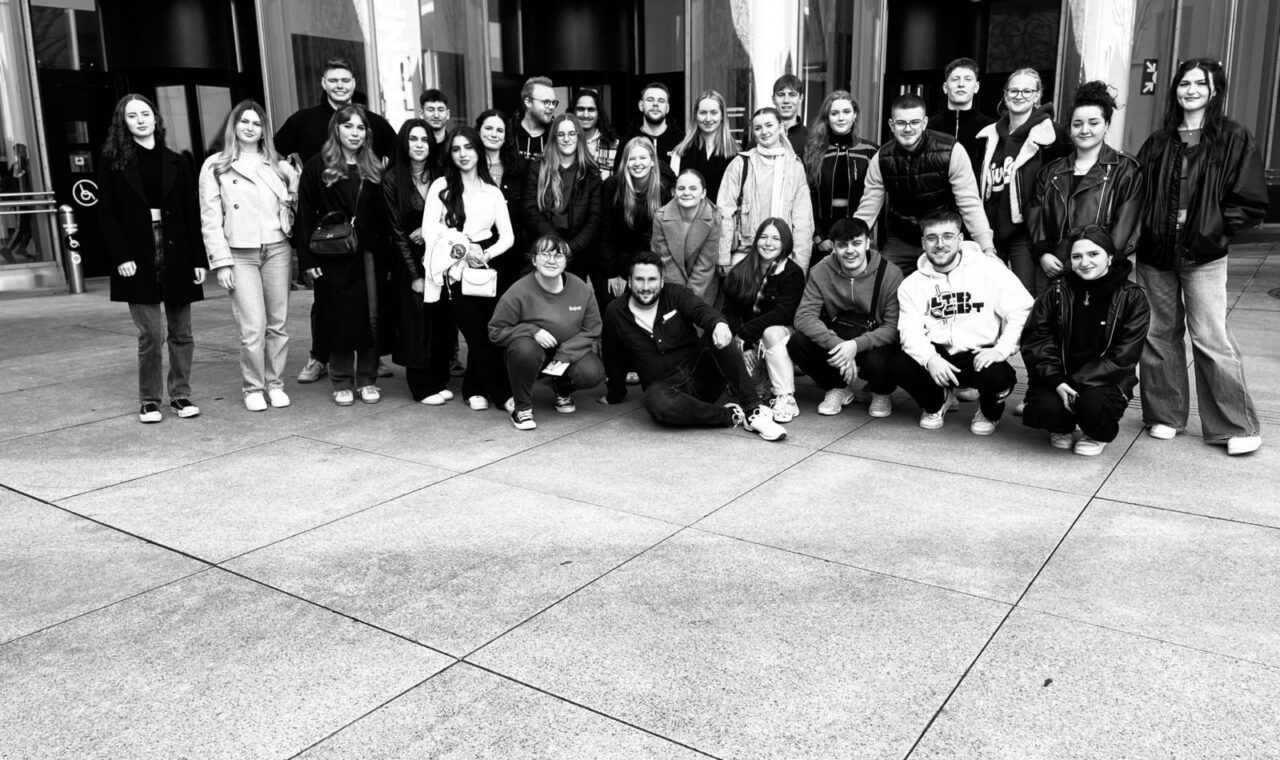 Gruppenfoto von Schülern und Lehrern vor einem Gebäude. Schwarz-weiß, freundliche Atmosphäre.