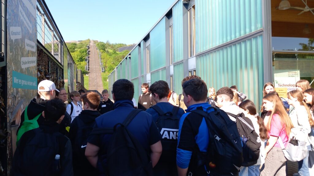 Gruppenschüler stehen vor einem Gebäude und hören einem Vortrag zu.