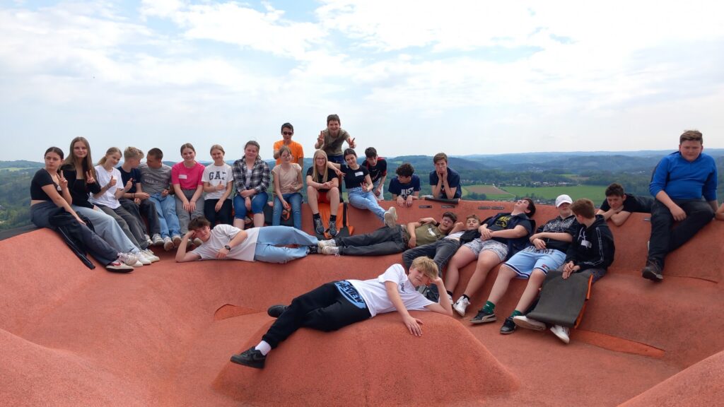 Gruppe von Schülern posiert auf einer großen, gewellten roten Fläche im Freien.