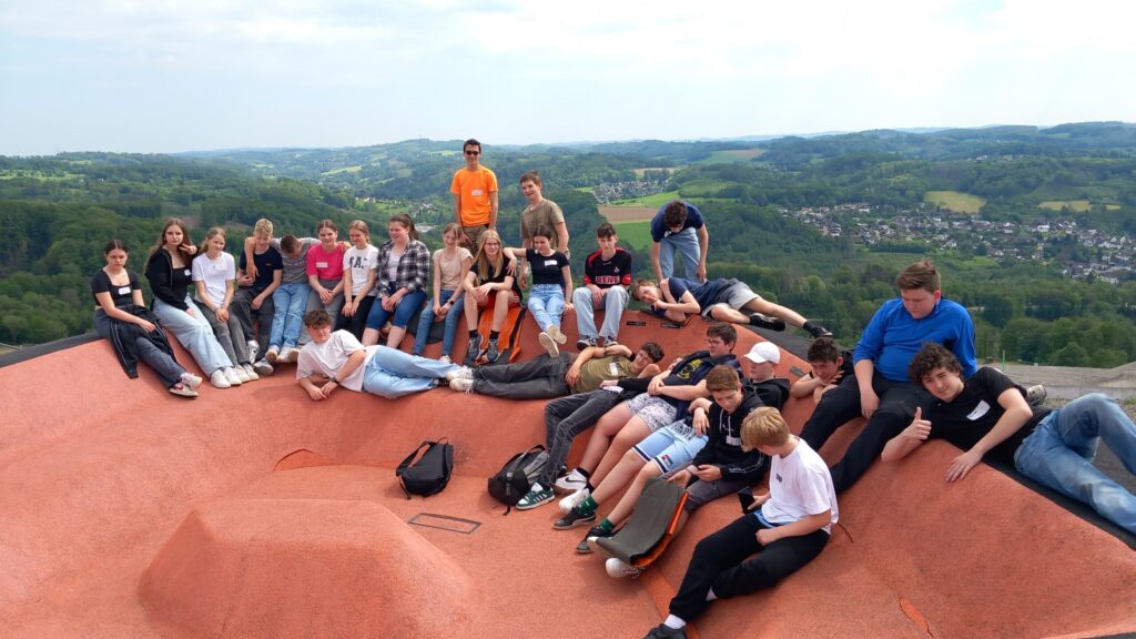 Gruppe von Schülern sitzt und steht auf einer großen roten Fläche mit Landschaft im Hintergrund.