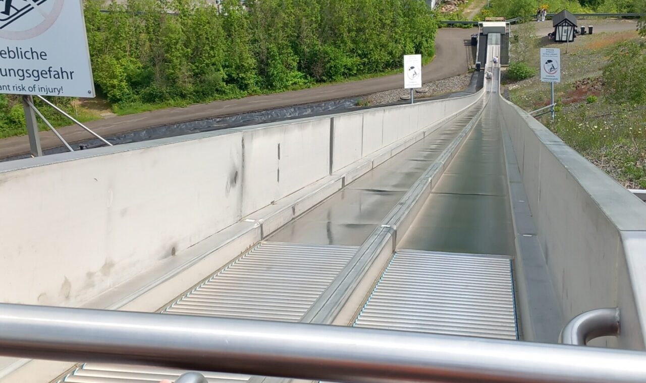 Blick auf eine Rodelbahn aus der Perspektive eines Fahrers. Wäldern im Hintergrund.