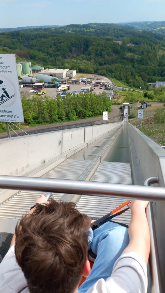 Blick auf eine Rodelbahn aus der Perspektive eines Fahrers. Wäldern im Hintergrund.