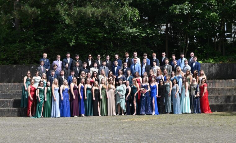Junge Frauen und Männer in formeller Kleidung stehen auf einer Treppe im Freien.