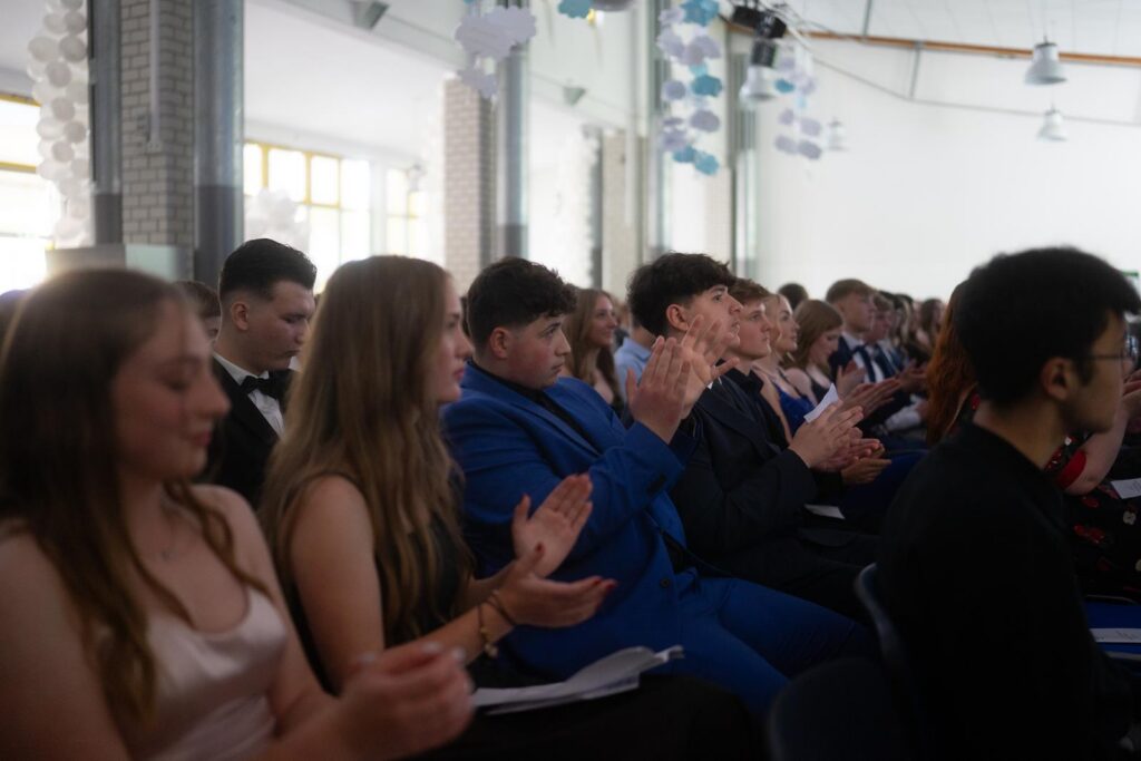 Schüler und Schülerinnen sitzen applaudierend in einem Festsaal.
