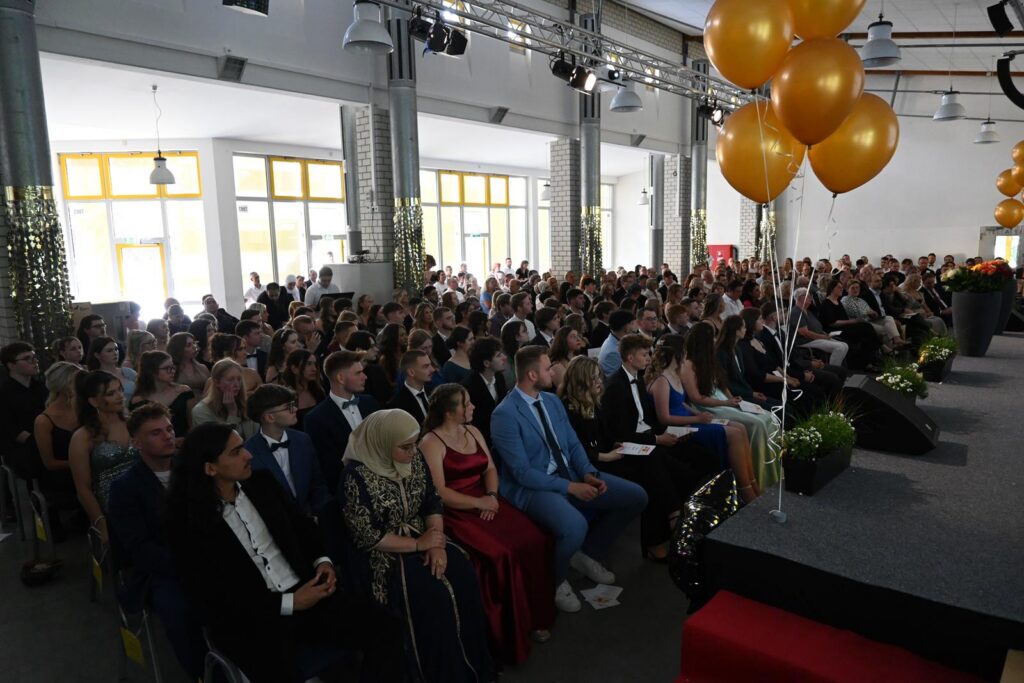 Festliche Veranstaltung mit vielen Gästen in elegantem Outfit und goldenen Ballons.