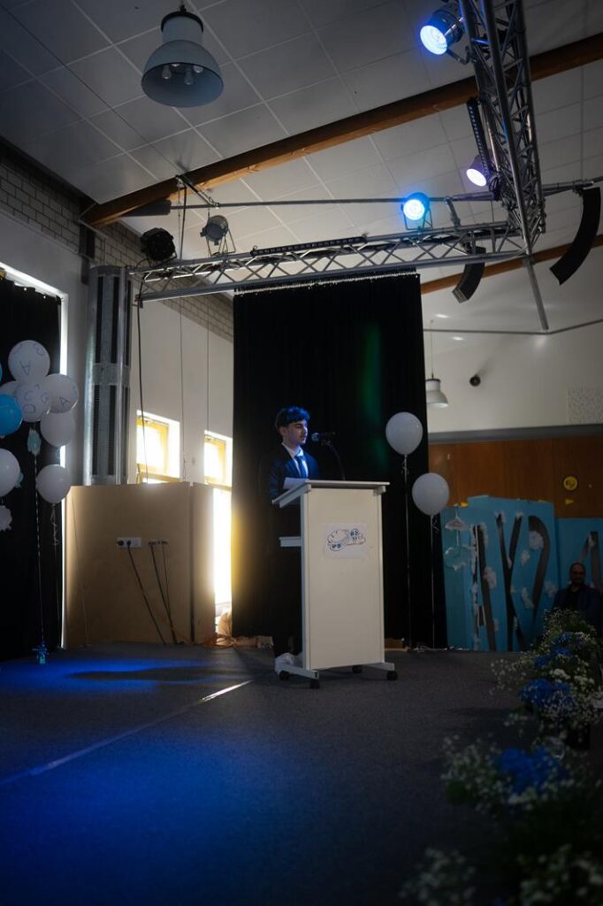 Ein Redner steht an einem Podium auf einer festlich dekorierten Bühne.