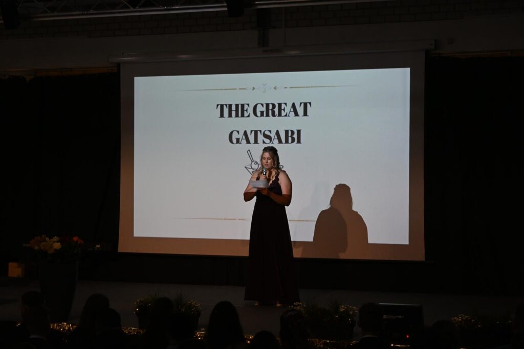 Schülerin steht auf der Bühne vor einer Präsentation des Titels "The Great Gatsby".