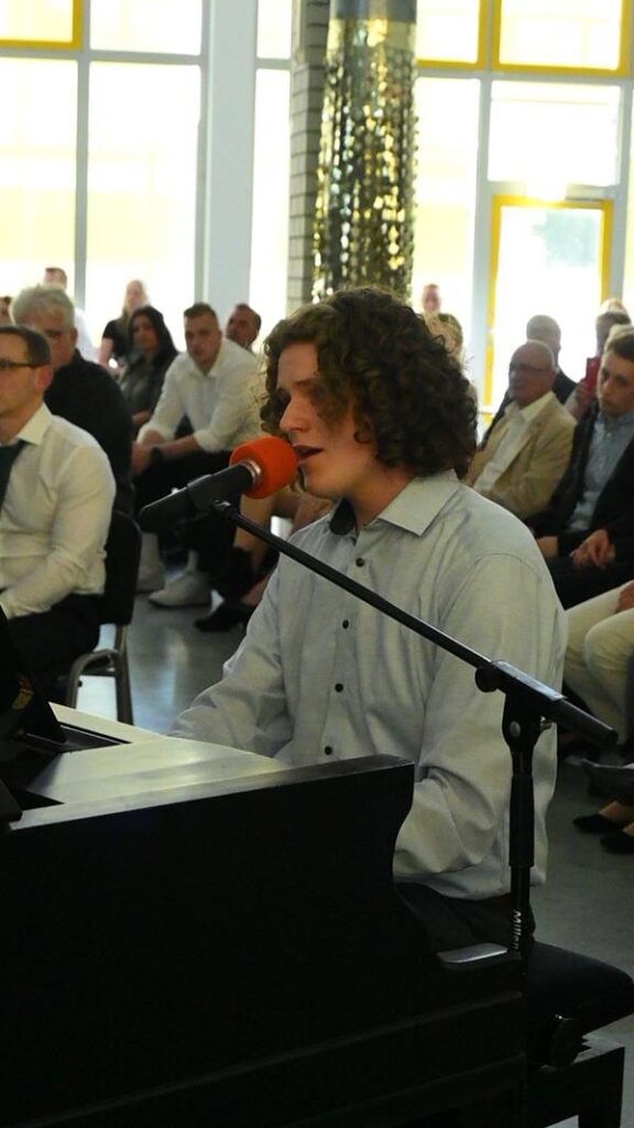 Schüler spielt am Klavier und singt vor Publikum in einem festlichen Raum.