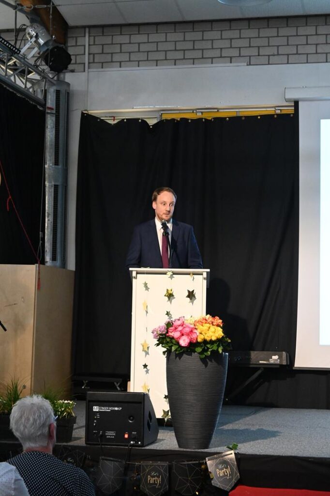 Ein Redner steht an einem Pult vor einer Präsentation und Pflanzen.