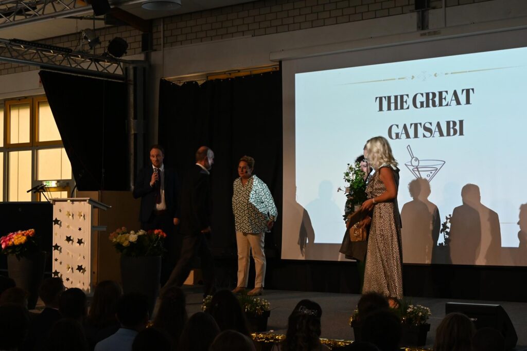 Auf der Bühne stehen vier Personen, im Hintergrund ein Bildschirm mit "THE GREAT GATSABI".