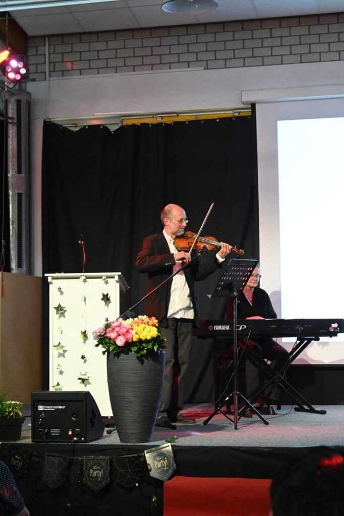 Ein Geiger spielt auf einer Bühne, im Hintergrund ein Keyboarder. Zuschauer sind sichtbar.