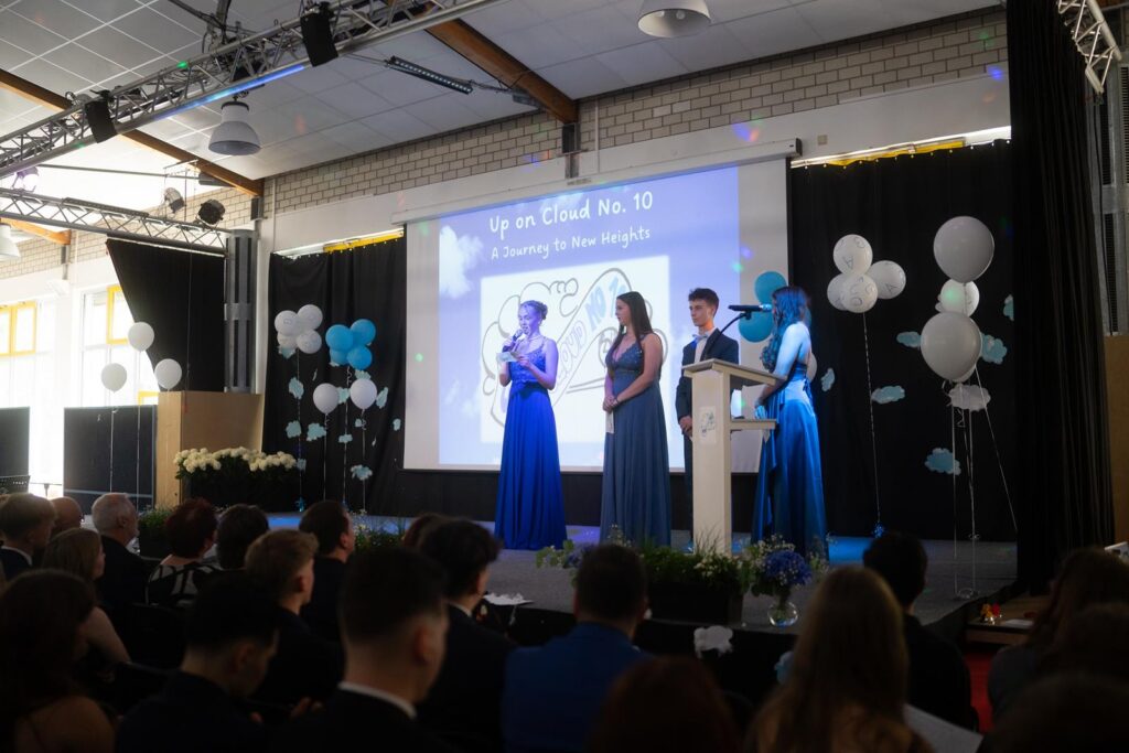 Ein festlicher Anlass mit vier Personen auf einer Bühne, Publikum im Vordergrund.