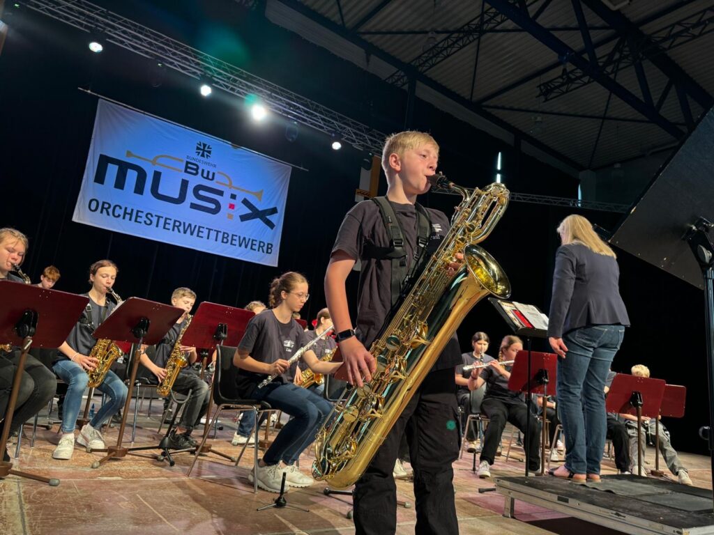 Ein Schüler spielt Euphonium vor einem Orchester während eines Wettbewerbs.