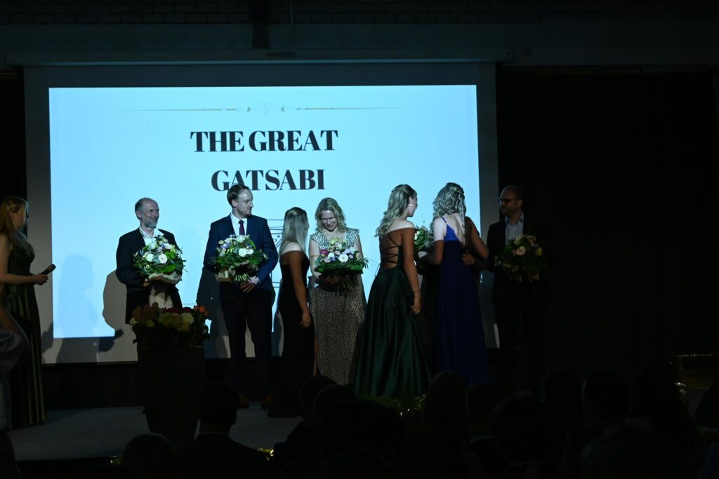 Veranstaltung mit mehreren Personen auf der Bühne, Blumenübergabe im festlichen Rahmen.