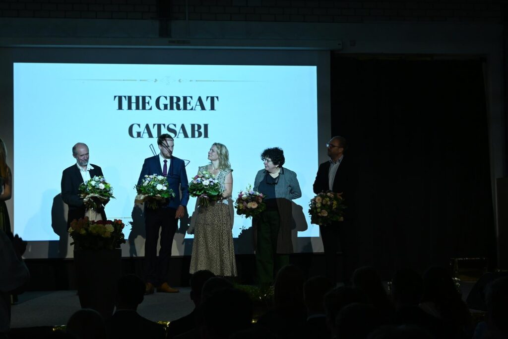 Veranstaltung auf der Bühne mit vier Personen und Blumensträußen.