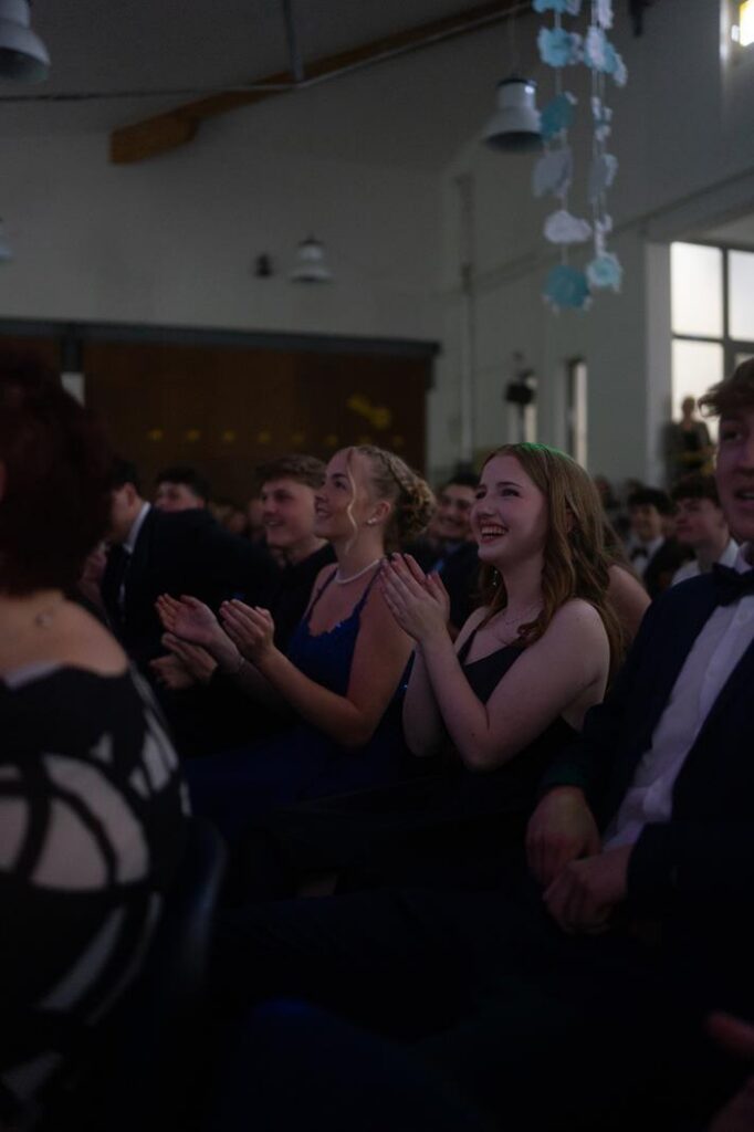 Schüler applaudieren in festlicher Kleidung bei einer Veranstaltung.