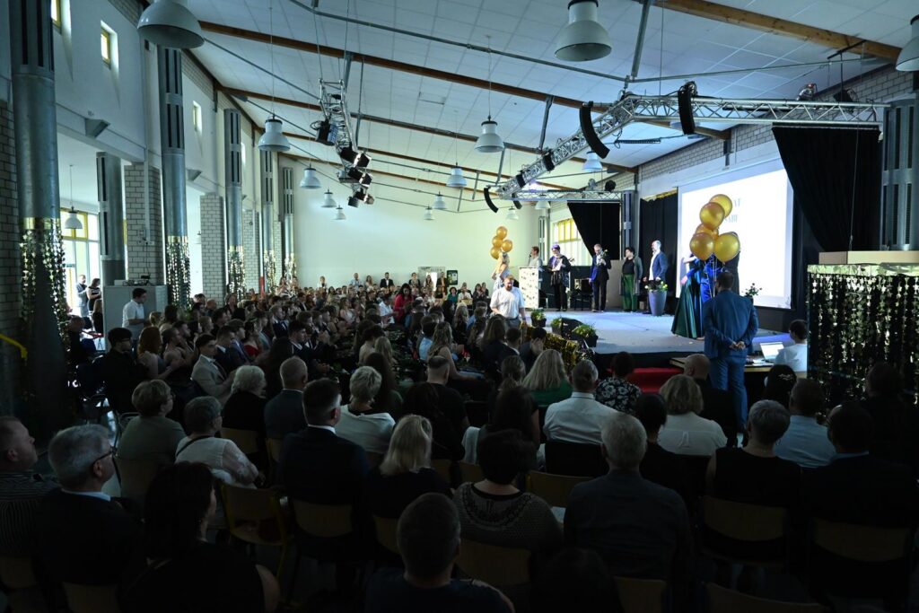 Vielbesuchte Veranstaltung in einem großen Saal mit Bühne und Zuschauern.
