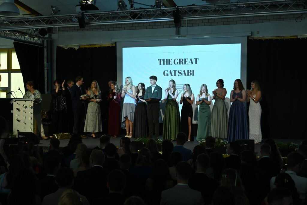Abschlussveranstaltung mit Gästen auf der Bühne und Publikum im Vordergrund.