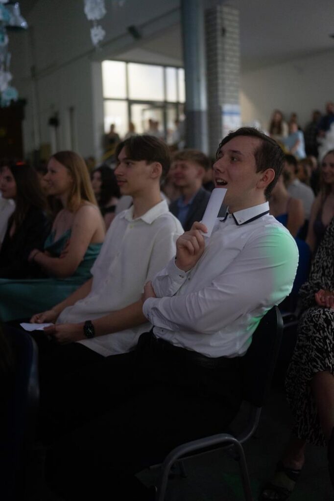 Zuschauer in einem Saal bei einer Veranstaltung, einige halten Karten in der Hand.