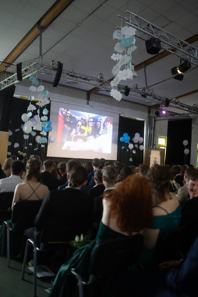 Schüler im Festsaal schauen auf eine große Leinwand.