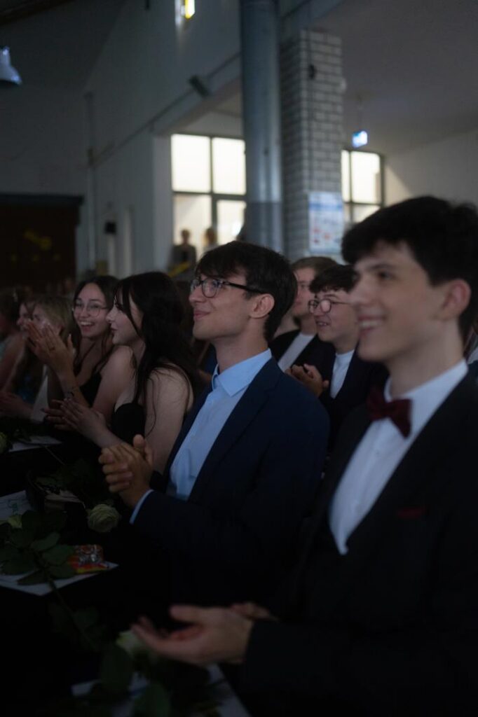 Gruppen von Schülern sitzen und applaudieren bei einer Veranstaltung.