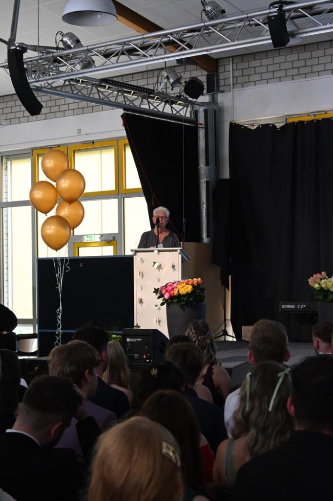 Veranstaltung mit Redner am Pult vor Publikum und Luftballons.