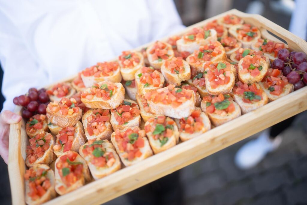 Ein Holztablett mit vielen Bruschetta und einigen Trauben.