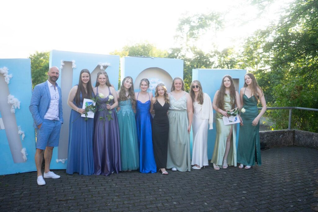 Gruppe junger Frauen in festlichen Kleidern vor einer dekorativen Kulisse.