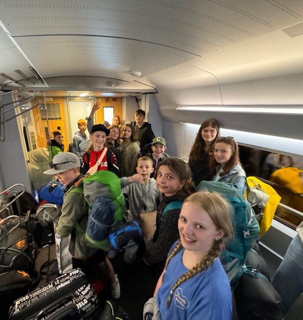 Gruppe von Schülern mit Rucksäcken in einem Transportfahrzeug.