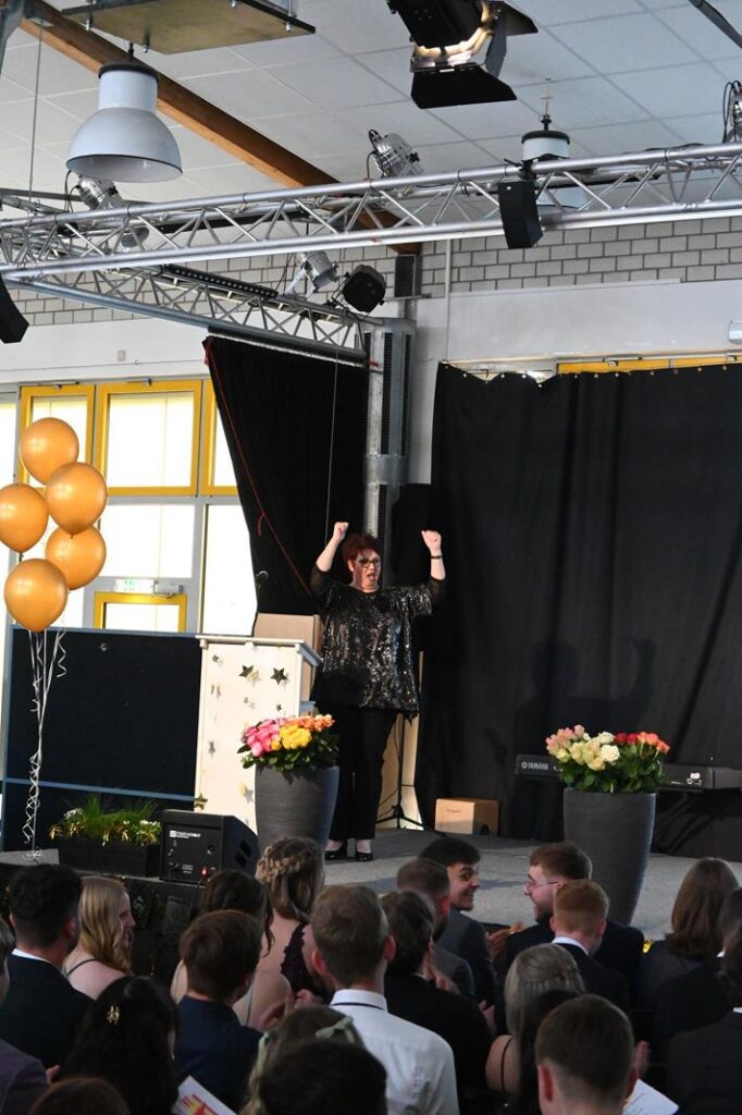 Veranstaltung in der Aula mit Leuten im Publikum und einer Rednerin auf der Bühne.