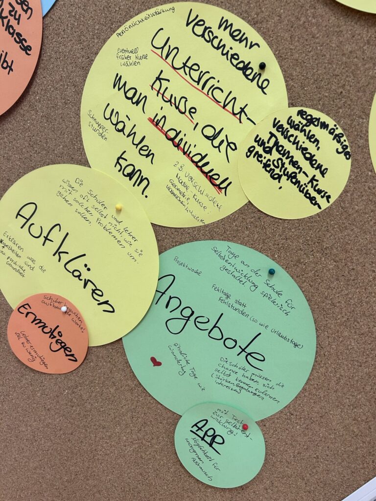 Bunte Zettel mit Texten zu Unterrichtsangeboten an einem Pinnwand.