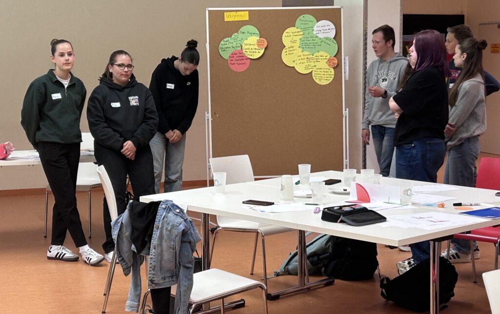 Gruppendiskussion mit Teilnehmern vor einem Tafelblatt in einem Seminarraum.