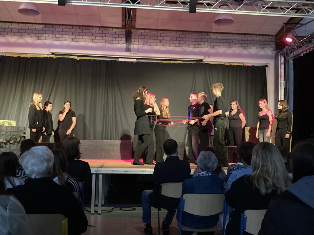 Schüler führen eine Theateraufführung auf einer Bühne vor Publikum auf.